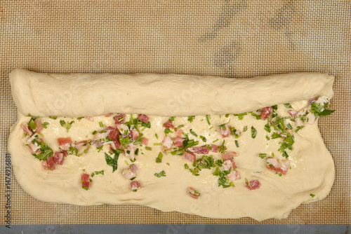 Obraz na płótnie Raw dough is being rolled up with a filling of diced pancetta and green herbs on a baking mat, in the process of making pancetta rolls w salonie