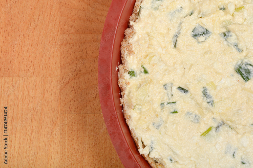 A top-down view shows a round cheese pie with fresh cheese and green onions in a red baking dish on a wooden surface
