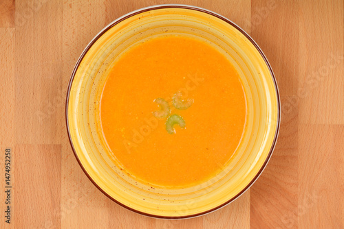 Obraz na płótnie A top-down view shows a creamy orange carrot soup garnished with celery in a yellow and brown bowl on a wooden surface w salonie