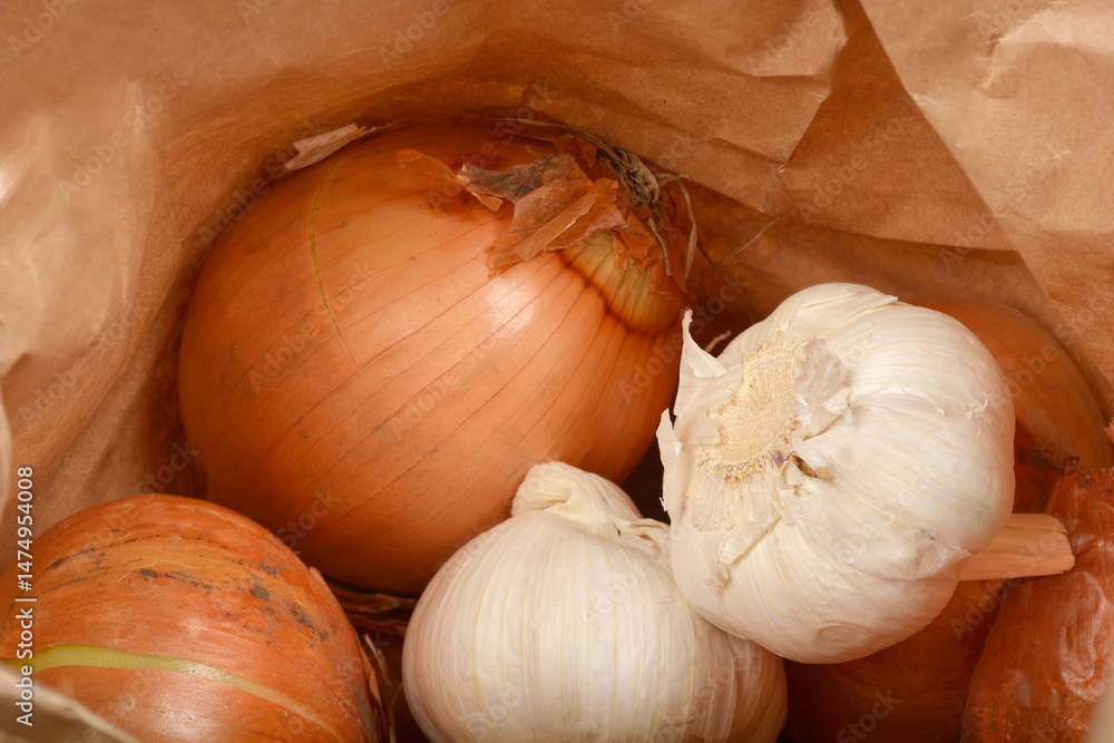 A close-up from inside a paper bag shows several brown onions and white garlic bulbs mixed together