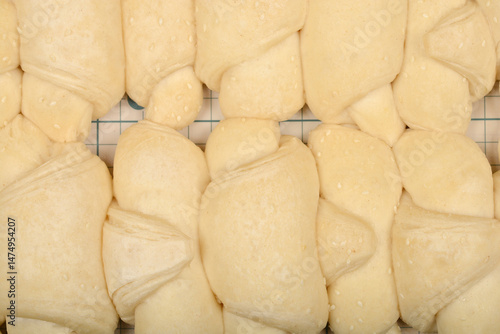 Obraz na płótnie A close-up overhead shot shows rows of raw, pale yellow mini croissants sprinkled with sesame seeds on a grid surface w salonie