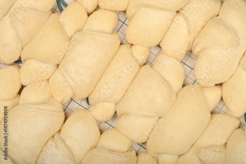 Obraz na płótnie A close-up overhead shot shows rows of raw, pale yellow mini croissants sprinkled with sesame seeds on a grid surface w salonie