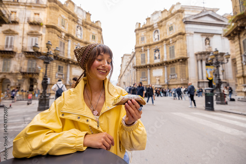 Fotografie A smiling woman in a yellow jacket enjoys a traditional Sicilian cannolo while sitting at a street cafe in Palermos historic center