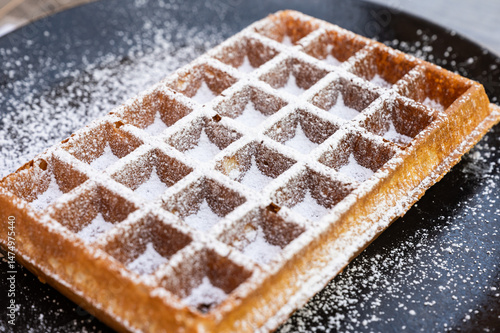Brussels waffle with icing sugar on a black plate in Hoeilaart, Flemish Brabant, Belgium
