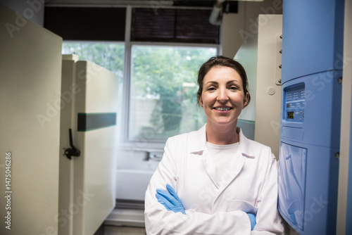 Smiling woman wearing lab coat and gloves in laboratory, highlighting freezer and control panel