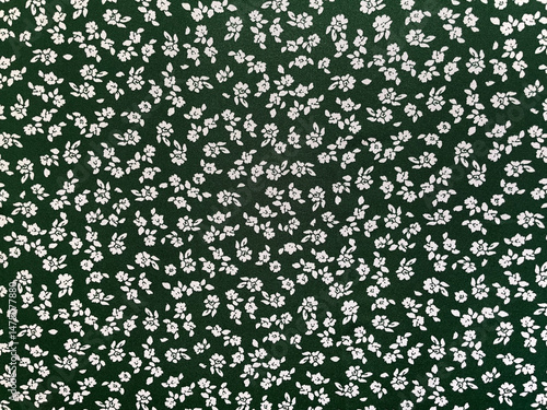 Fabric with seamless vintage small floral pattern, close-up as texture. Old-fashioned, retro style cotton or linen textile with print of scattered small white flowers on green background