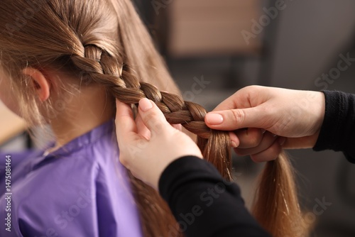 Schilderij op canvas Hairstylist braiding girl's hair in salon, closeup