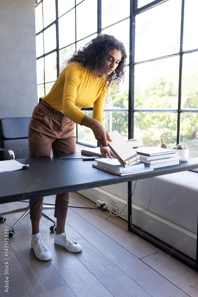 Obraz premium Organizing documents on office desk, businesswoman concentrating near large window