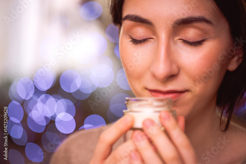 Photos Close-up of a pretty young woman with smooth skin sniffing a jar of moisturizer