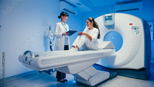 Engaged woman sitting on MRI bed talking with medical specialist before diagnostic scan. Doctor holding clipboard explaining procedure while patient responds calmly in hospital imaging room.