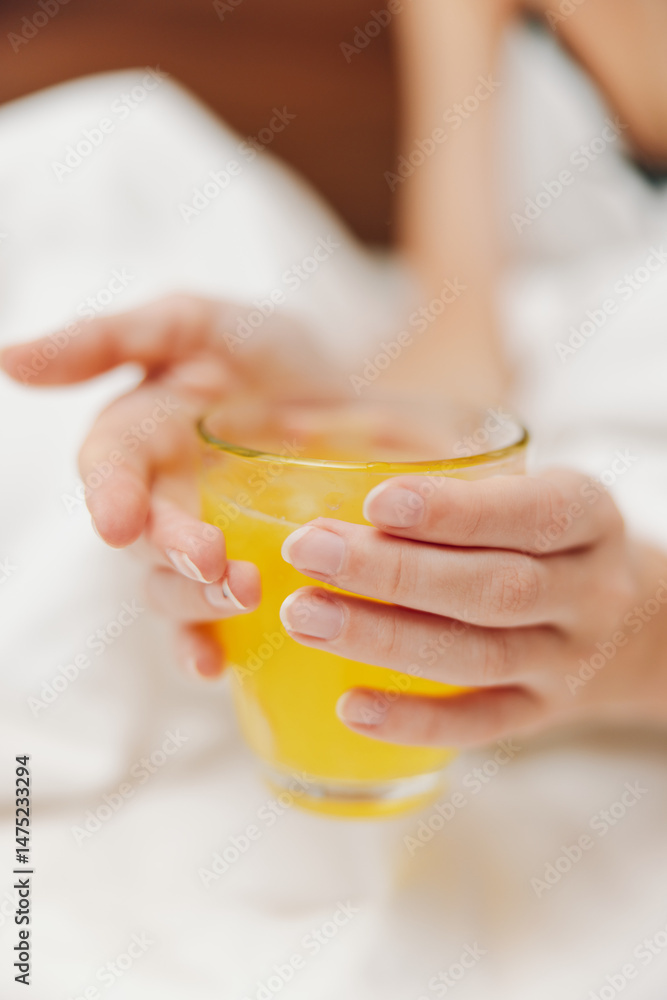 Woman holding glass of orange juice in bed with white sheet Woman holding glass of orange juice in bed with white sheet
