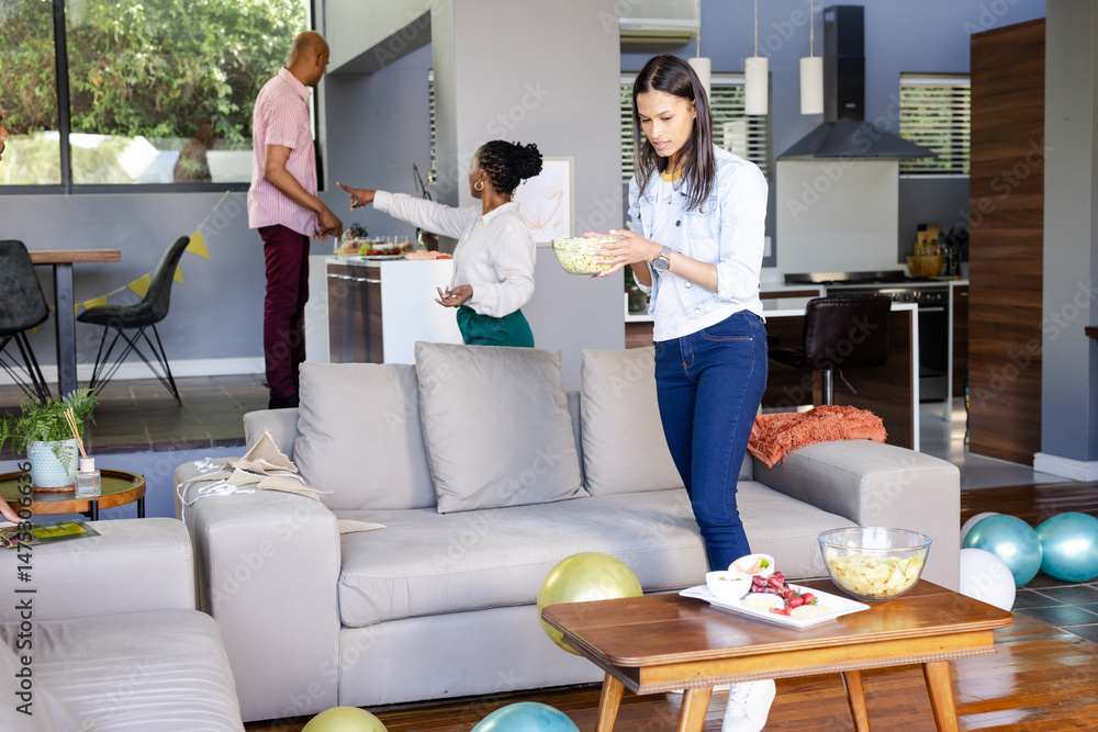 Obraz premium Woman preparing snacks in living room while friends setting up for celebration