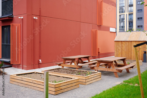 contemporary communal outdoor space with picnic tables and planters by modern red building. urban gardening concept promotes community interaction and sustainable living in shared environments