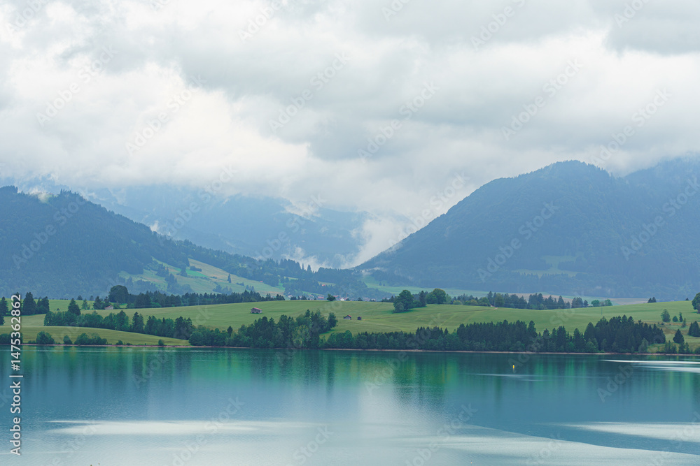 Mountain landscape with serene lake reflecting cloudy sky and lush greenery in the foreground at midday Mountain landscape with serene lake reflecting cloudy sky and lush greenery in the foreground at midday