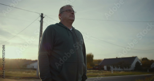 Wallpaper Mural Man standing on rural road at dusk with serene expression, sunset glow in background, rural scene, peaceful moment, open landscape, solitude in countryside Torontodigital.ca