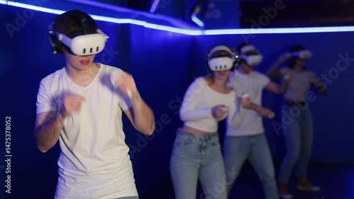 Wallpaper Mural In darkened hall of gaming club, guy in VR helmet takes part in group game. Player overcomes obstacles and reaches goal in parallel reality. Imaginary fantastic world  Torontodigital.ca