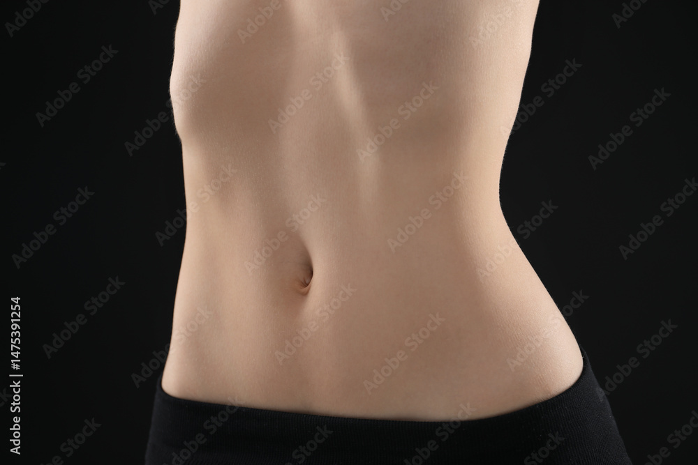 Naklejka premium Attractive woman against black background, closeup on belly