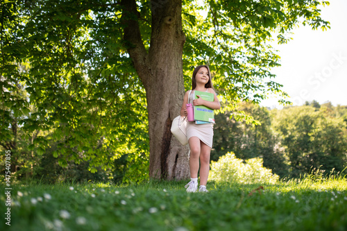 Fotografie Child walking in park with backpack and bools in hands book on sunny day