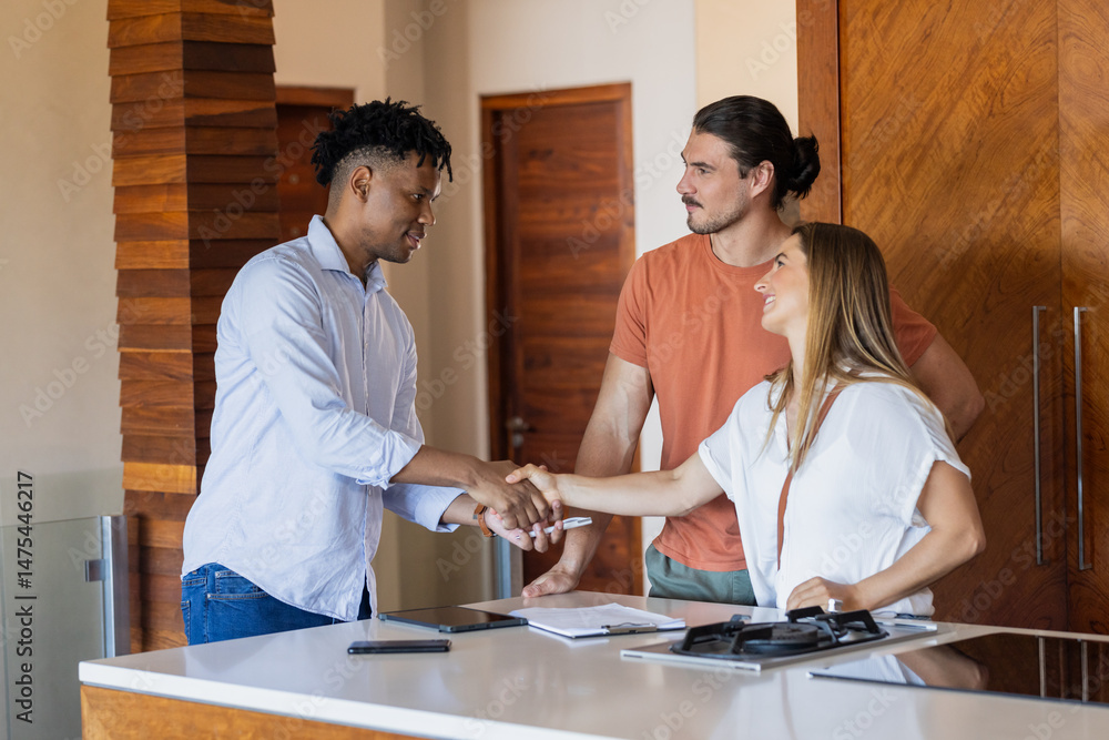 Fototapeta premium Real estate agent shaking hands with couple in modern kitchen, finalizing agreement