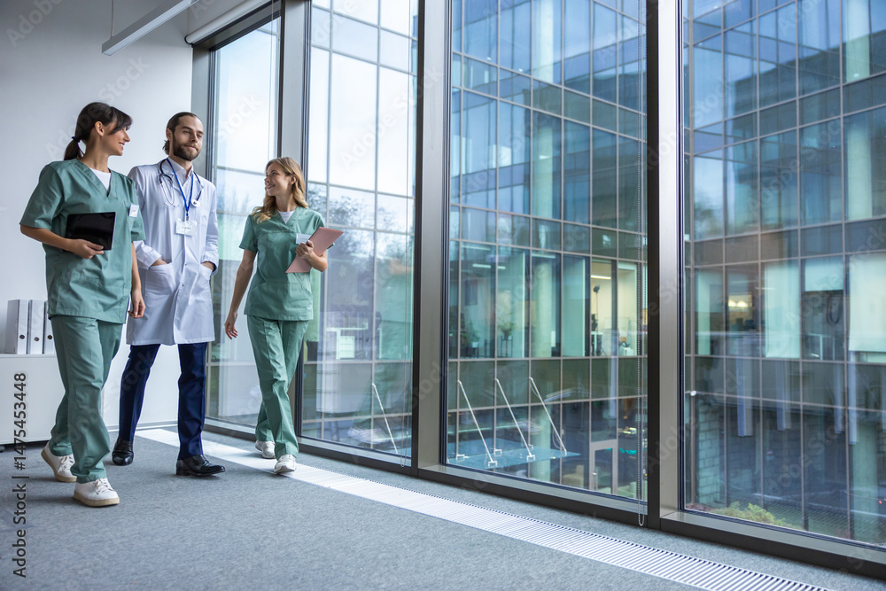 Fototapeta premium Group of young doctors in lab coats walking in the clinic corridor and talking