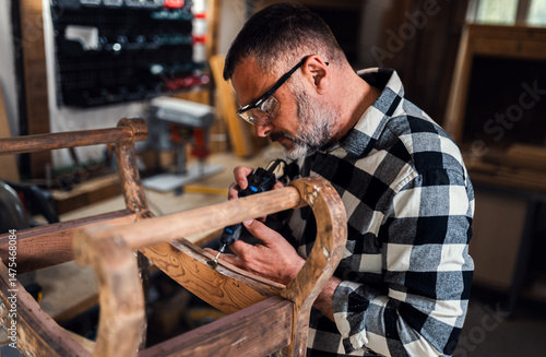 Carpenter standing in his workshop restoring old piece of furniture with mini grinder.