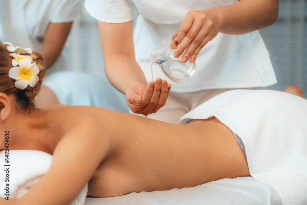 Fototapeta premium Masseur hands pouring aroma oil on couple's back. Masseuse prepare oil massage procedure for customer at spa salon in luxury resort. Aroma oil body massage therapy concept. Quiescent
