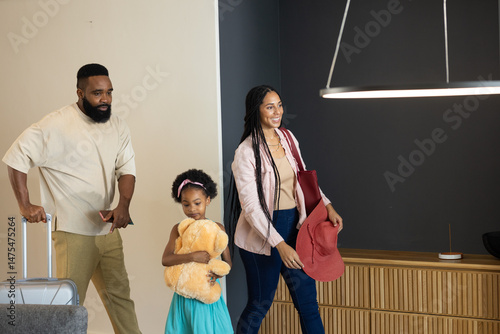 Family arriving home, smiling and carrying luggage and stuffed toy together
