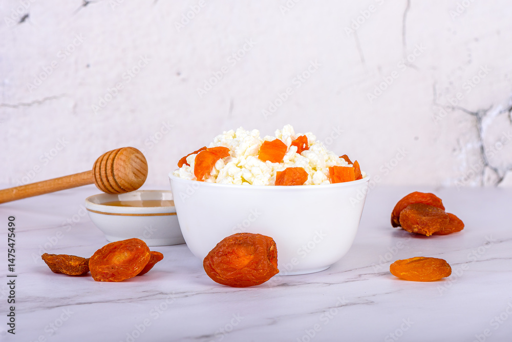 Fototapeta premium Fresh cottage cheese with dried apricot pieces and honey in a white bowl.