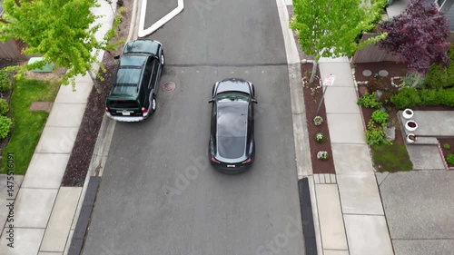 Aerial view of a gray car driving through a suburban neighborhood arriving at home; drone follow shot