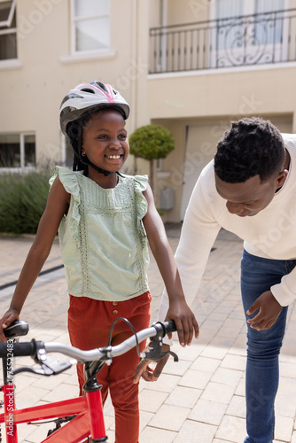Teaching daughter to ride bicycle, father guiding her outdoors, both smiling