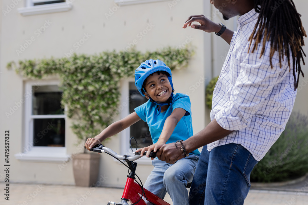 Obraz premium African American father teaching son to ride bicycle outside, both smiling happily