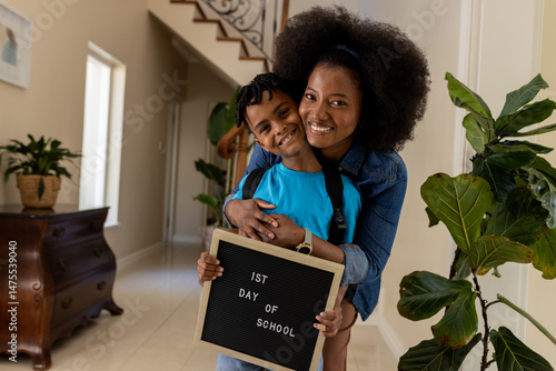 Mother and son smiling, holding sign for first day of school at home
