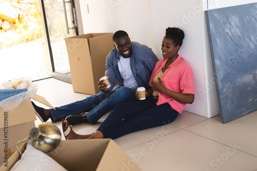 Couple sitting on floor enjoying coffee break while unpacking moving boxes at home