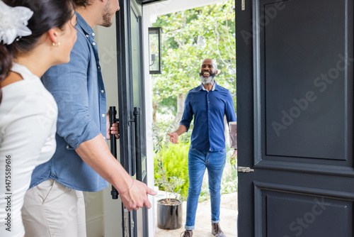 Welcoming guest at home, smiling couple greeting friend at front door