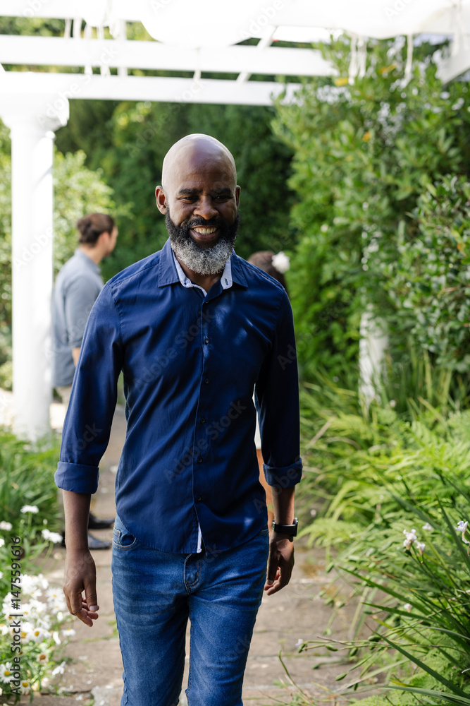 Fototapeta premium Smiling African American man walking through garden at wedding celebration
