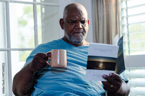 Senior man enjoying quiet time reading book and drinking coffee at home