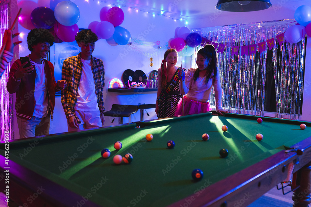 Fototapeta premium Teens enjoying birthday party playing pool in festive, colorful room with balloons