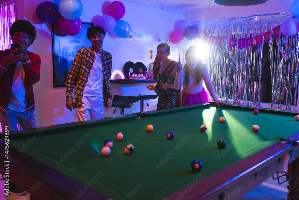 Fototapeta premium Teens celebrating birthday playing pool in festive room with colorful balloons