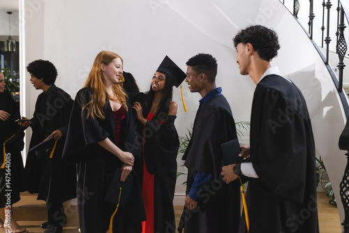 Teens in graduation gowns celebrating together, smiling and chatting indoors