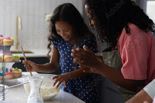 Mother and daughter baking together in kitchen, mixing ingredients with joy