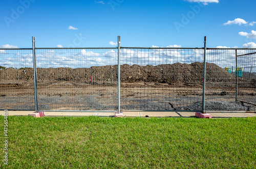 Construction site behind temporary fencing with dirt piles and leveled ground in suburban Australia—concept of land development, infrastructure preparation, and urban expansion.