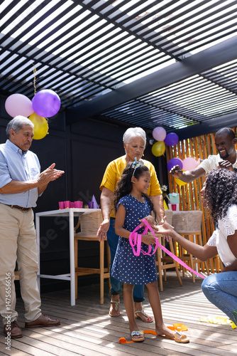 Family celebrating birthday with balloons and gifts, smiling and clapping together