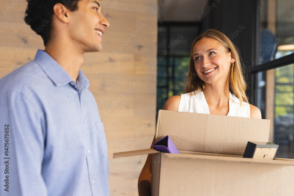 Colleagues smiling while carrying moving boxes in modern office setting Colleagues smiling while carrying moving boxes in modern office setting