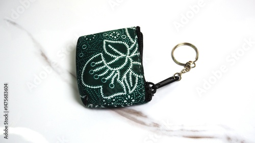 A close-up of a hand-carved keychain made from green stone, decorated with white floral patterns.