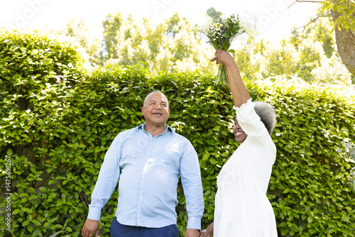 Senior couple enjoying sunny day outdoors, woman playfully holding bouquet up high