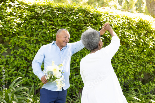 Senior couple dancing joyfully in garden, holding bouquet of fresh flowers