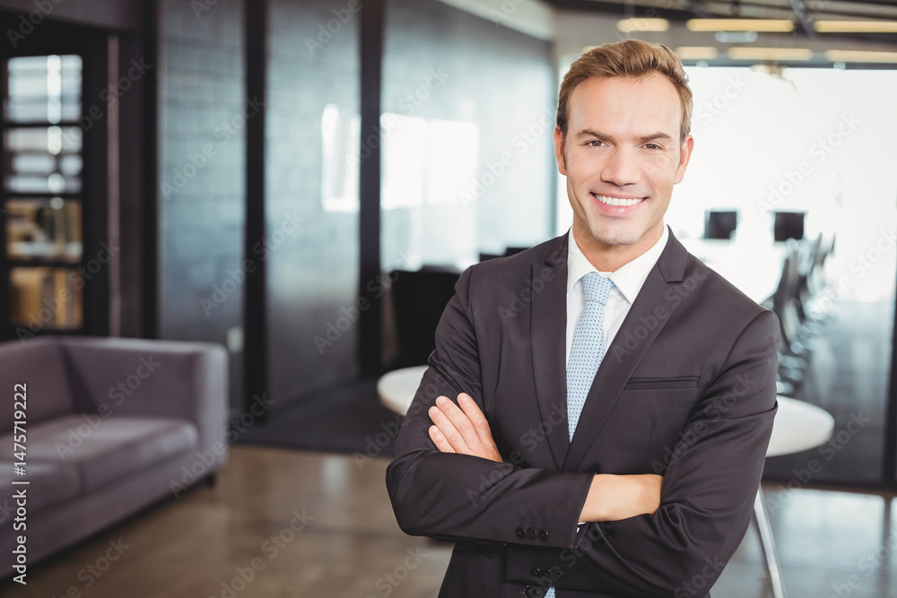 Fototapeta premium Standing middle-aged man wearing black suit crossing arms in open-plan office, glass partitions