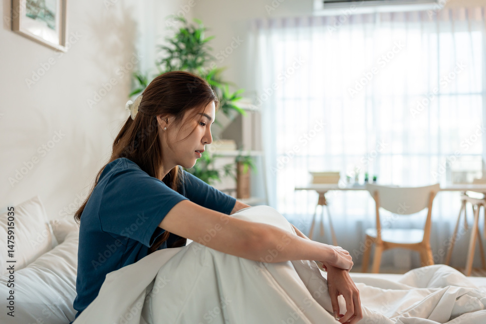 Obraz premium Depressed Asian young woman feel upset while sitting on bed in bedroom. 