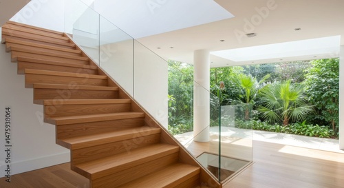 Modern interior design with wooden stairs and glass railing overlooking lush garden