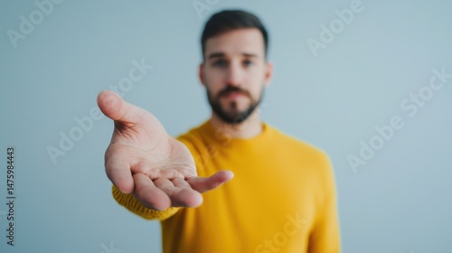Man in yellow sweater with outstretched hand looking at camera in bright studio setting